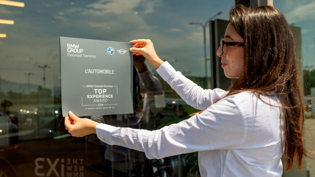 Vediamo una ragazza che applica la targa adesiva del Top Experience Award 2026 alla vetrina della Concessionaria